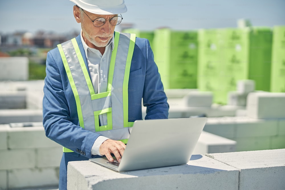 Front view of a focused civil engineer typing on a computer placed on the bricks