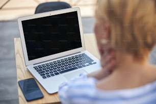 Rückansicht einer Freelancerin, die vor ihrem Laptop an einem Holztisch sitzt