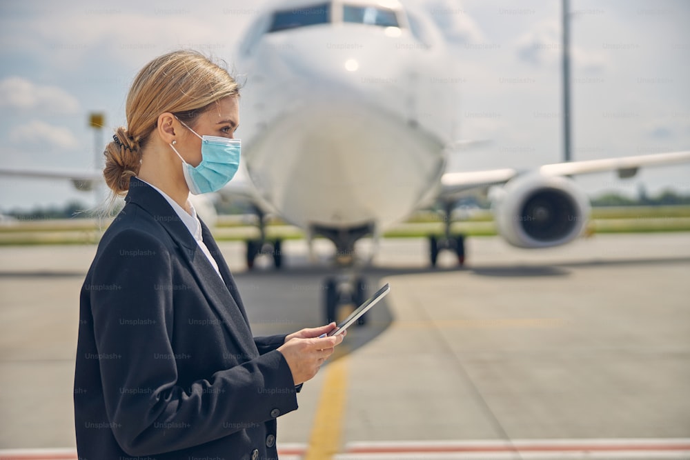 Side view of a young blonde Caucasian woman wearing a protective mask at the airport
