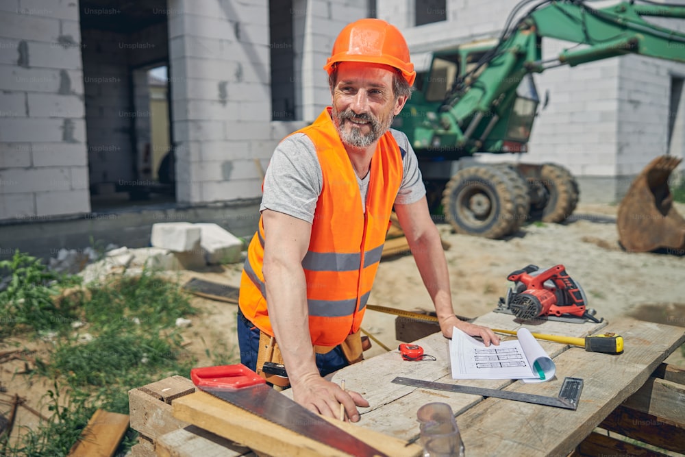 Smiling attractive civil engineer leaning his hands on a wooden table at a building site