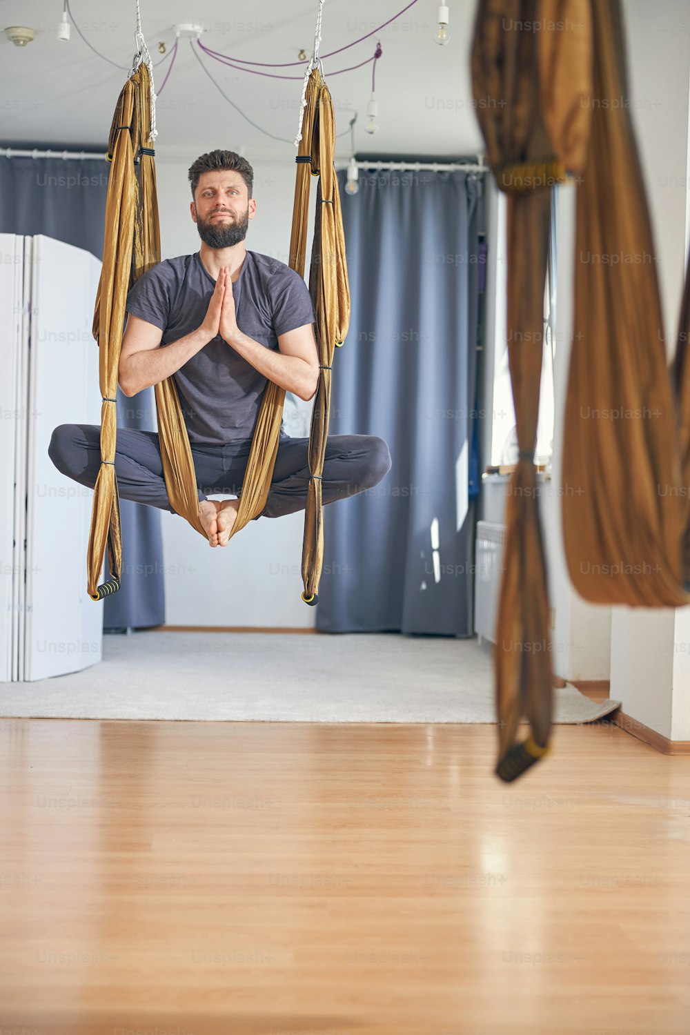 Front view of a tranquil professional yogi with clasped hands hanging in a silk hammock