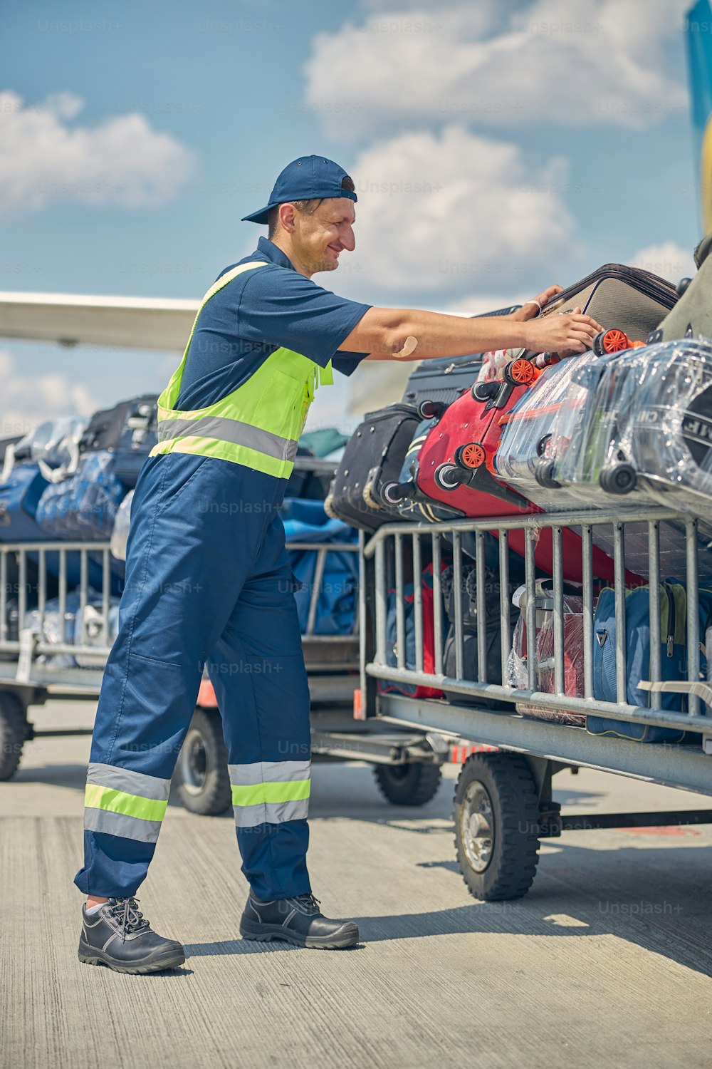 Portrait en pied d’un bagagiste sérieux chargeant les bagages des clients sur des chariots à l’aérodrome