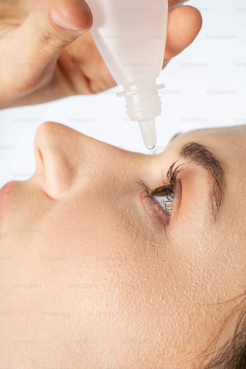 Close up of female hand holding white bottle and dripping eye drops on eye