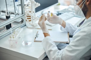 Photo recadrée d’un virologue vêtu d’une blouse de laboratoire et de gants en latex examinant des vaccins contre le coronavirus