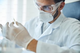 Concentrated scientist in safety goggles and latex gloves staring at the test tube in his hand