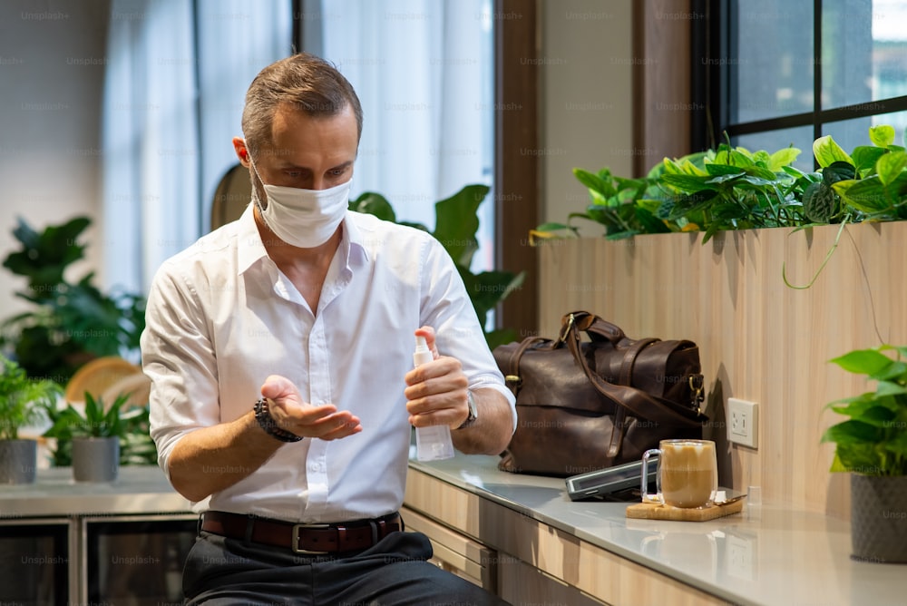 Portrait of Caucasian man wearing face mask and using hand sanitizer spray washing his hands in coffee shop.