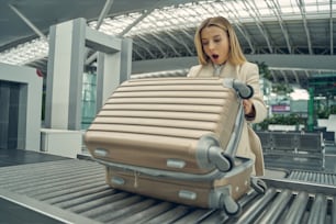 Surprised young woman keeping her mouth opened while doing check-up of her luggage