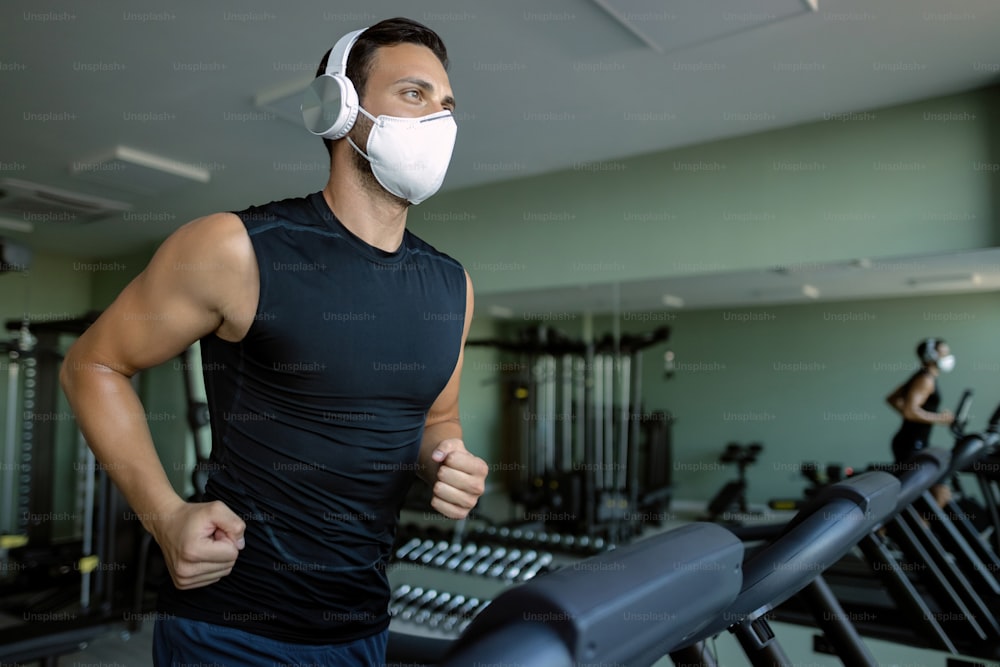 Joven deportista con una máscara facial mientras corre en la cinta de correr en el gimnasio durante la epidemia de coronavirus.