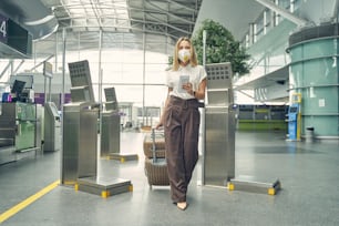 Kind blonde woman holding her ticket while looking straight at camera, going for registration on flight