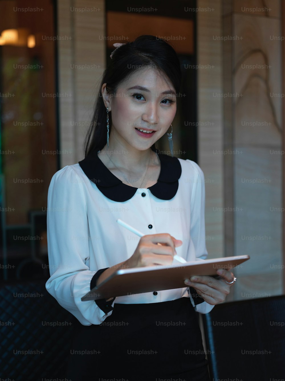 Portrait of businesswoman standing in conference room, looking into camera while working with digital tablet