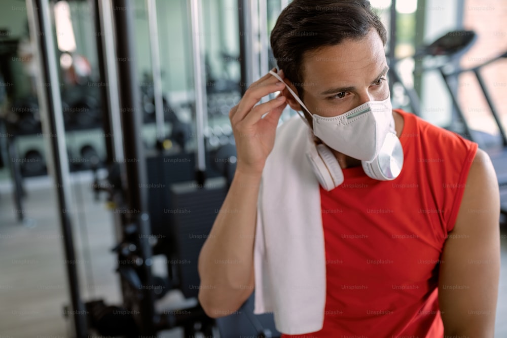 Male athlete exercising in health club and putting on a face mask due to coronavirus epidemic.