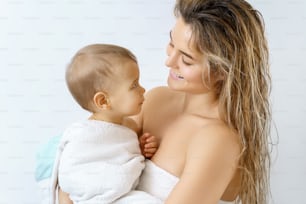 Igiene e cura del bambino. Madre giovane e felice e suo figlio neonato carino dopo il bagno.