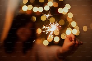 Menina elegante com brilho ardente celebrando no quarto escuro festivo. Feliz Ano Novo. Mulher feliz segurando fogos de artifício na árvore de Natal com luzes douradas.