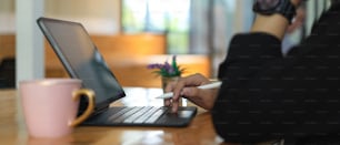 Vista lateral de una mujer independiente que trabaja con una tableta digital en una mesa de trabajo con una taza de café en un espacio de trabajo conjunto