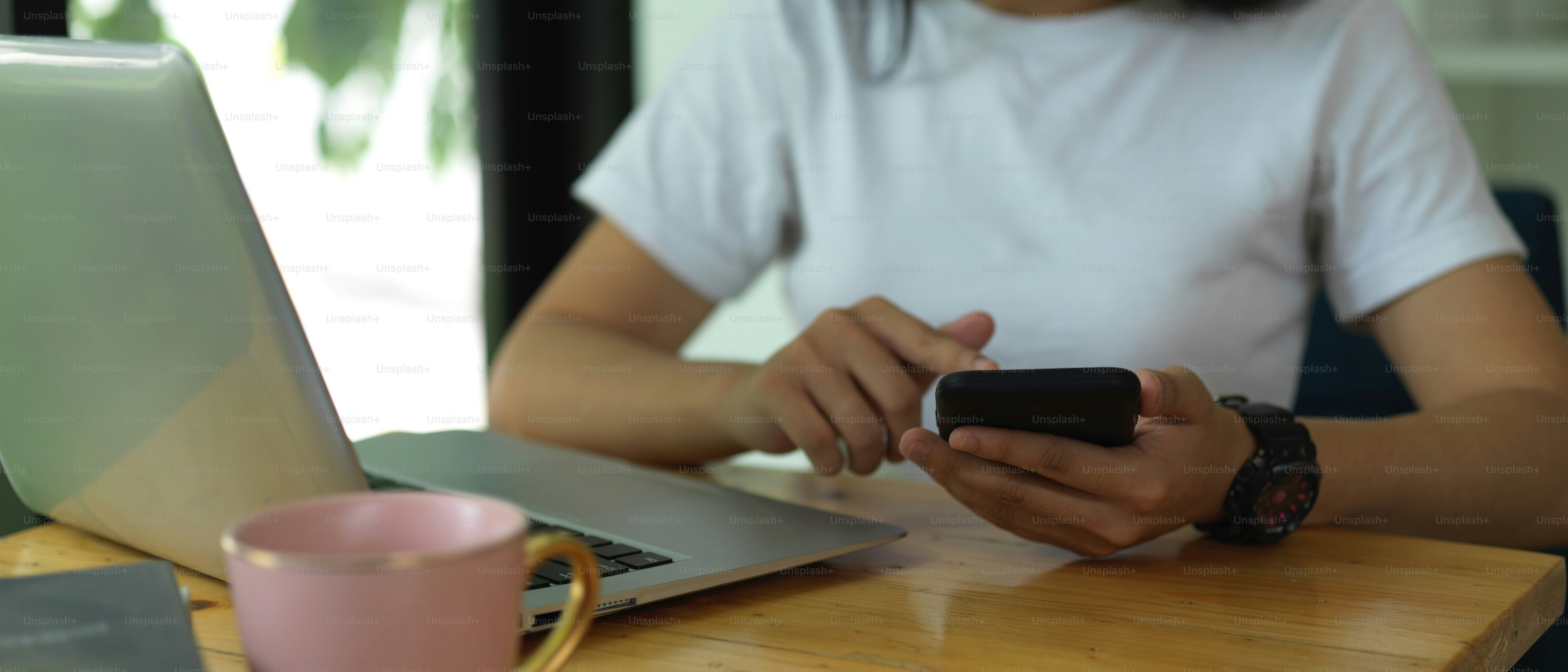 Cropped shot of female university student using smartphone while doing assignment with laptop in cafe