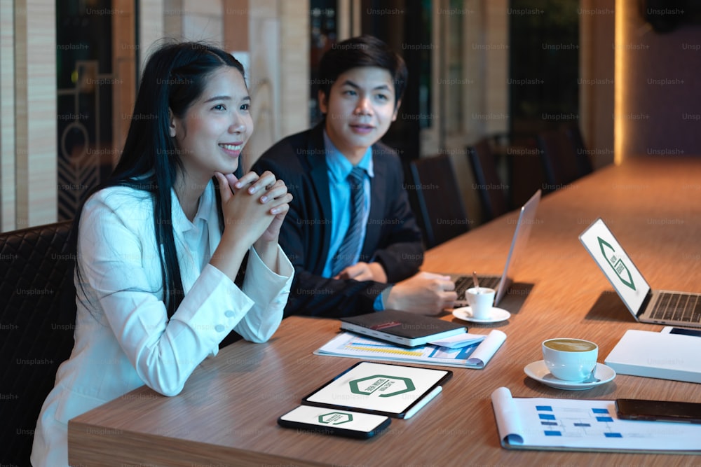 Portrait of cheerful businesspeople sitting at meeting table with digital devices and paperwork