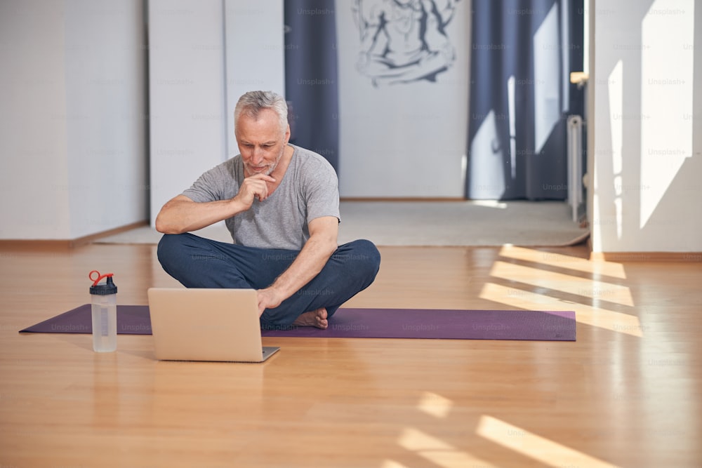 Vista frontal de un hombre deportivo sentado con las piernas cruzadas en la alfombra de yoga