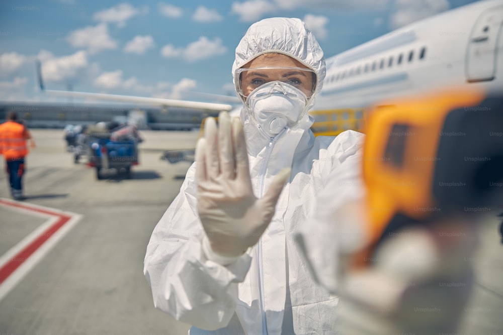 Waist-up portrait of a woman in a hazmat suit making a stop sign with her hand