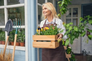 Smiling contented mature blonde woman with a wooden box of flowers staring into the distance