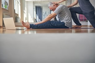 Vista lateral de um yogi iniciante realizando um exercício de alongamento assistido por seu personal trainer