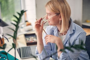 Peaceful blonde female fixing her glasses while resting at work desk