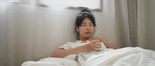 Uma mulher doente bebe água e consome uma pílula enquanto está deitada na cama do quarto.