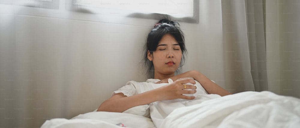 Una mujer enferma bebe agua y consume una pastilla mientras está acostada en la cama del dormitorio.