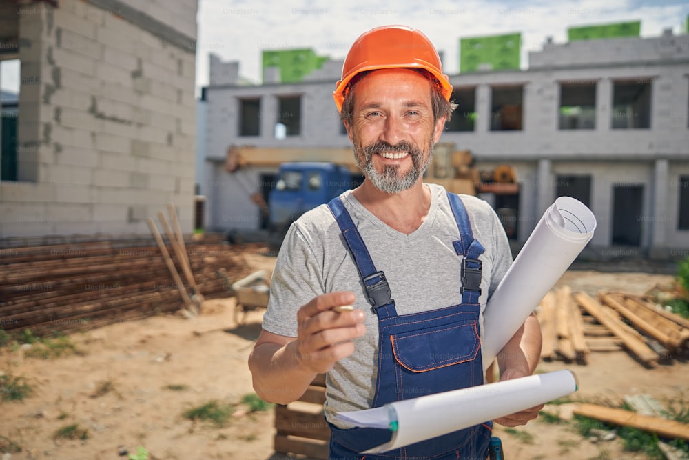 Front view of a merry mature civil engineer with house plans posing for the camera