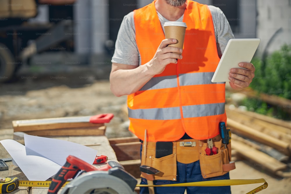 Cropped photo of a Caucasian man in workwear holding a tablet computer in his hand