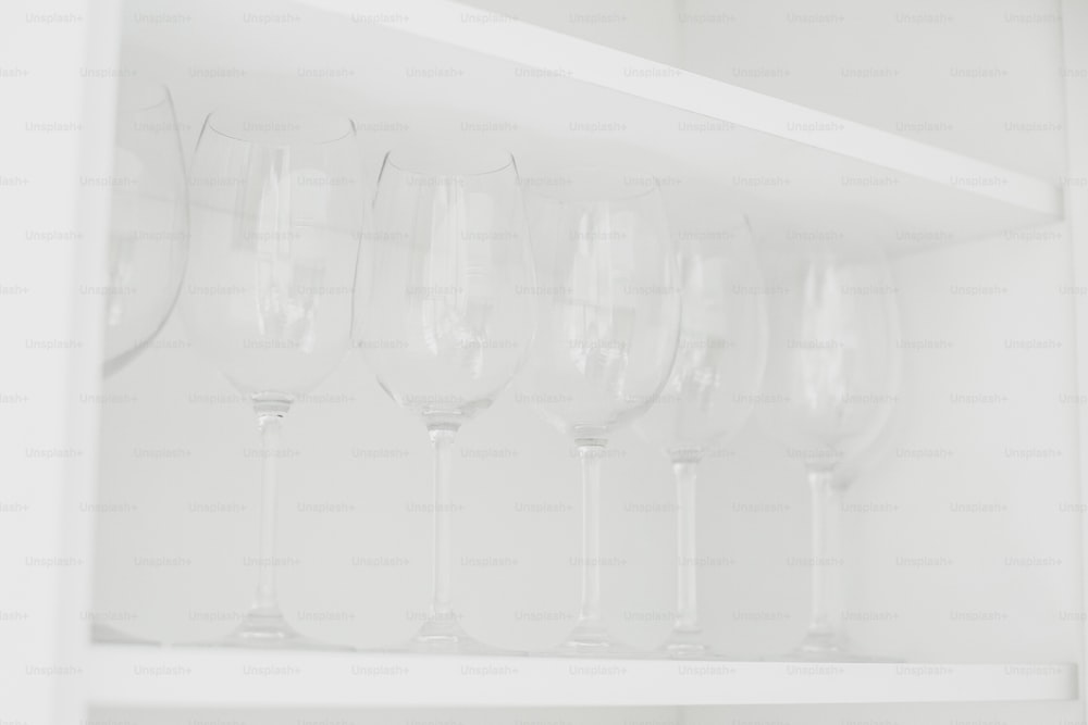 Transparent glasses on white shelf in modern white kitchen. Row of clean crystal wineglasses. Clean dishes at hotel or home