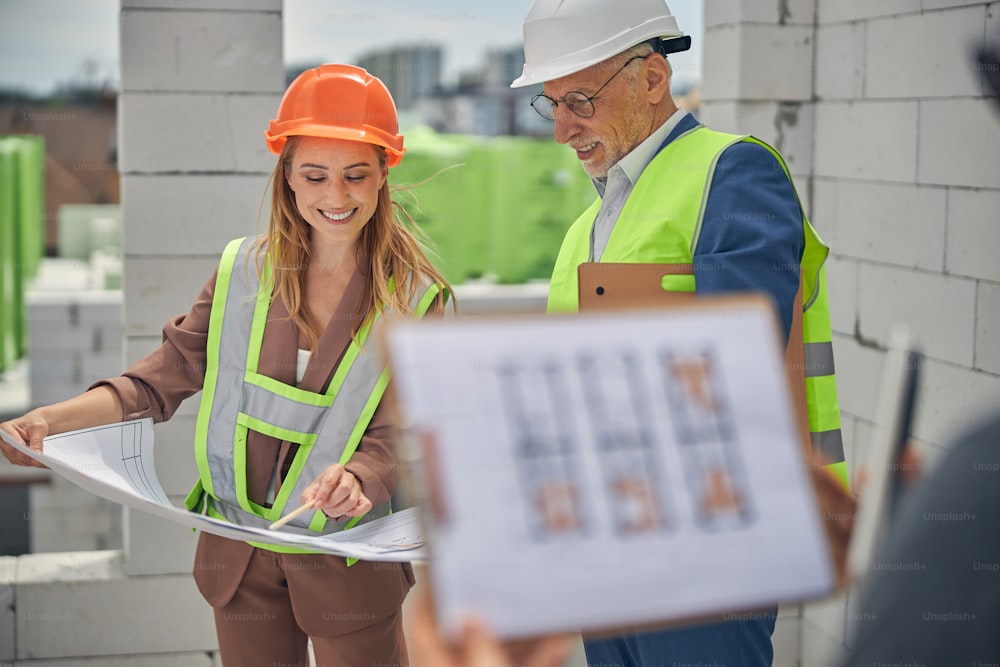 Smiling blonde woman engineer pointing at a technical drawing to a pleased senior construction supervisor