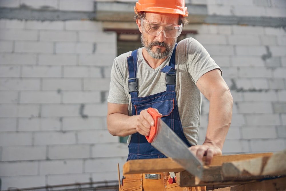 Front view of a focused joiner in safety goggles cutting off a piece of wood