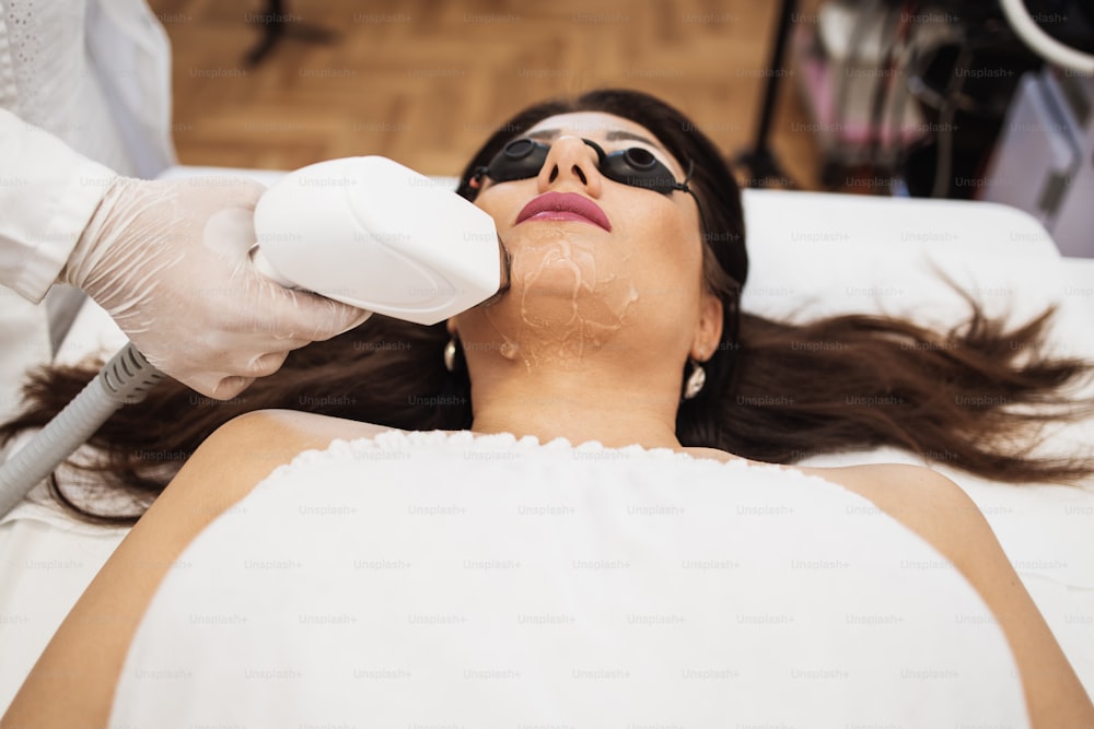 Young beautiful woman receiving face skin epilation treatment. Modern body care and cosmetics concept.