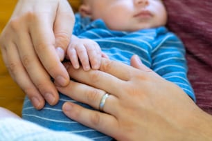 Close up of Caucasian family father and mother with newborn baby son are holding hands together.