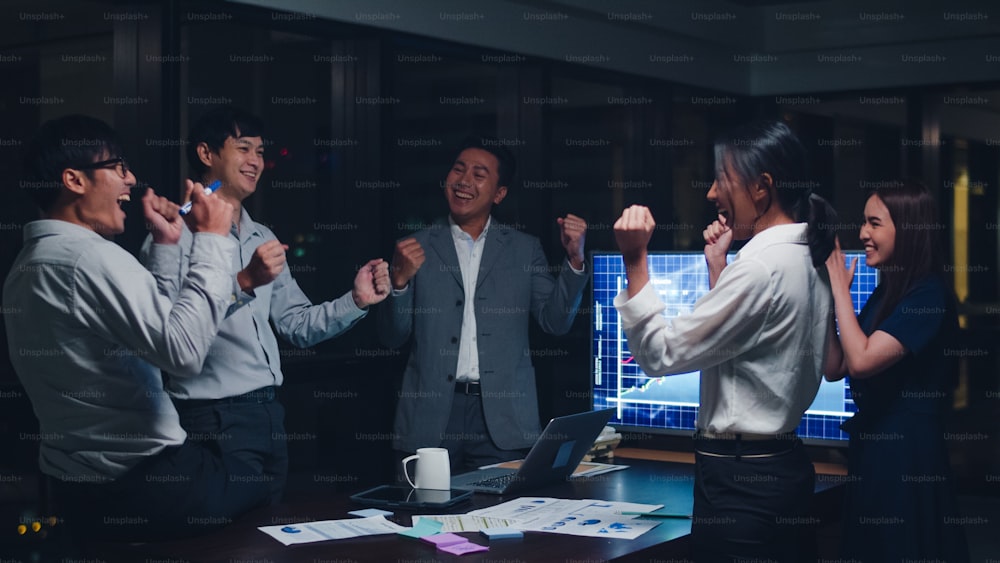 Millennial group of young businesspeople Asia businessman and businesswoman celebrate giving five after dealing and signing contract or agreement at meeting room at small modern night office in city.