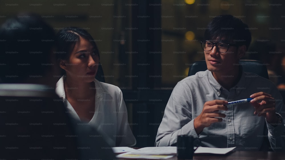 Millennial Asia businessmen and businesswomen meeting brainstorming ideas about new paperwork project colleagues working together planning success strategy enjoy teamwork in small modern night office.