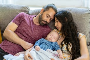 Familia feliz dos padres con bebé recién nacido descansando juntos en el sofá de la sala de estar