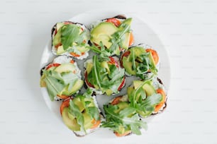 Plate with homemade toasts with avocado on modern white kitchen. Sandwich made of whole grain bread, avocado, tomato, arugula and cheese, top view. Home cooking concept