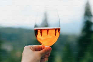 Main tenant un délicieux cocktail à l’orange sur fond de montagnes, de vacances d’été et de villégiature. Femme applaudissant avec une boisson aperol, célébrant à l’extérieur