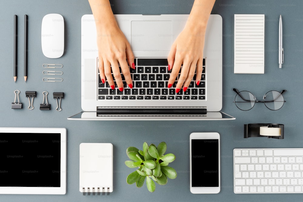 Weibliche Hände arbeiten auf modernem Laptop auf grauem Hintergrund mit Zubehör. Office-Desktop. Flache Liege