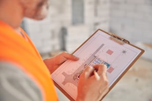 Cropped photo of a qualifed Caucasian civil engineer drawing with a pencil on the clipboard