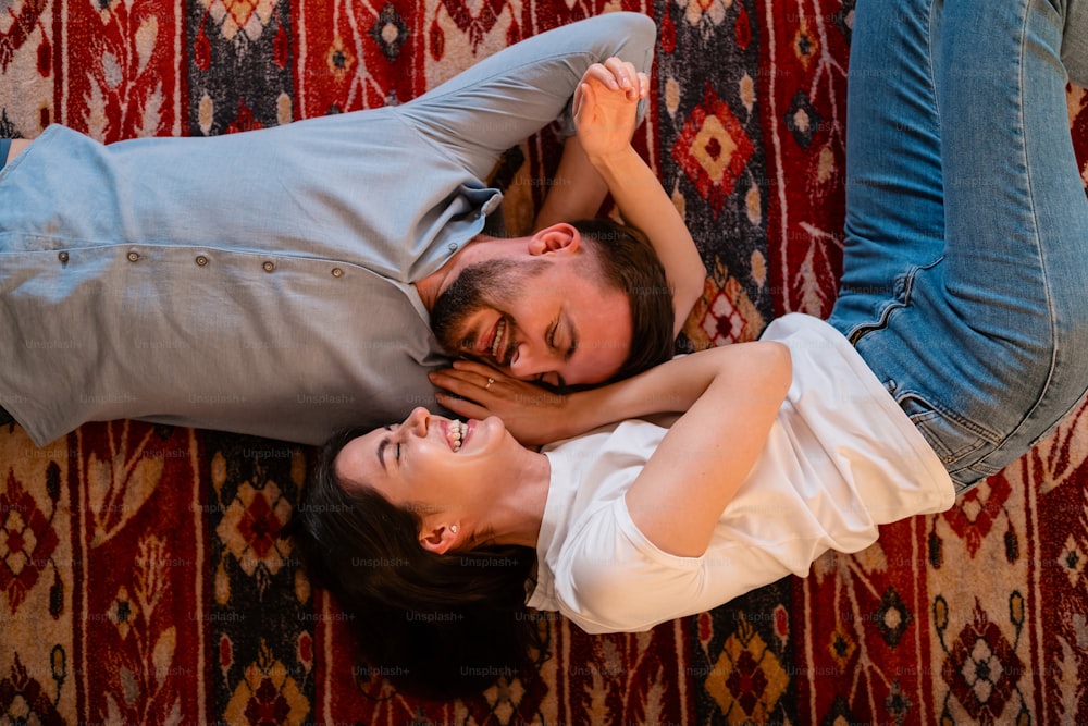 Top view young charming couple looking to each other smiling while lying on a colorful carpet with folk ornaments