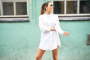 Beautiful tourist enjoying city streets. Girl wearing fashionable sunglasses and white dress.