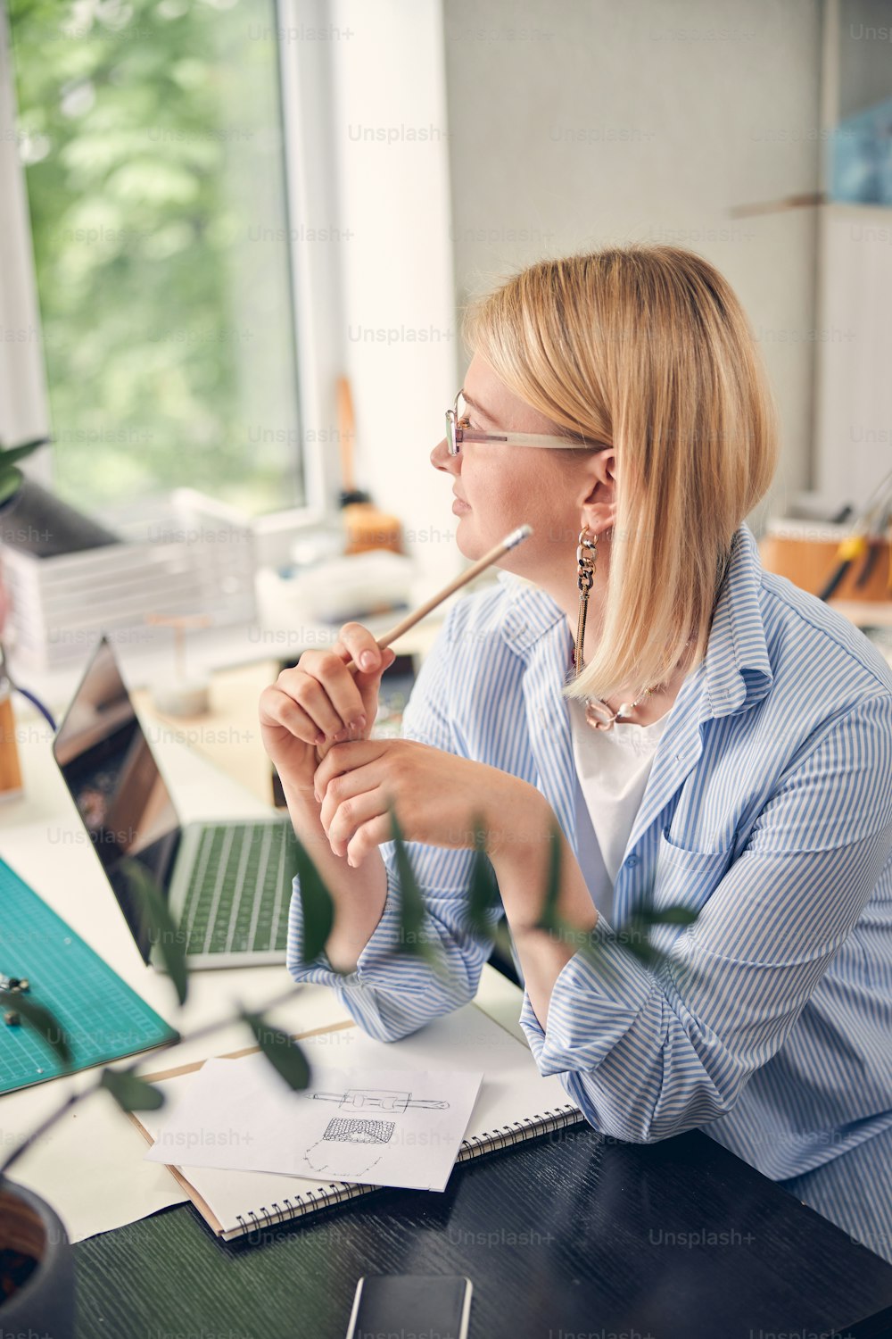 Smart designer glancing away while holding a pencil and working on new sketch