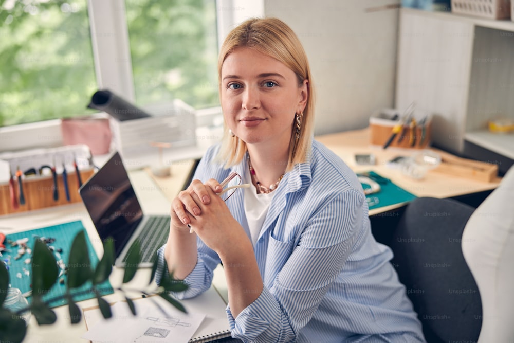 Skilled designer keeping glasses in both hands while sitting at the table