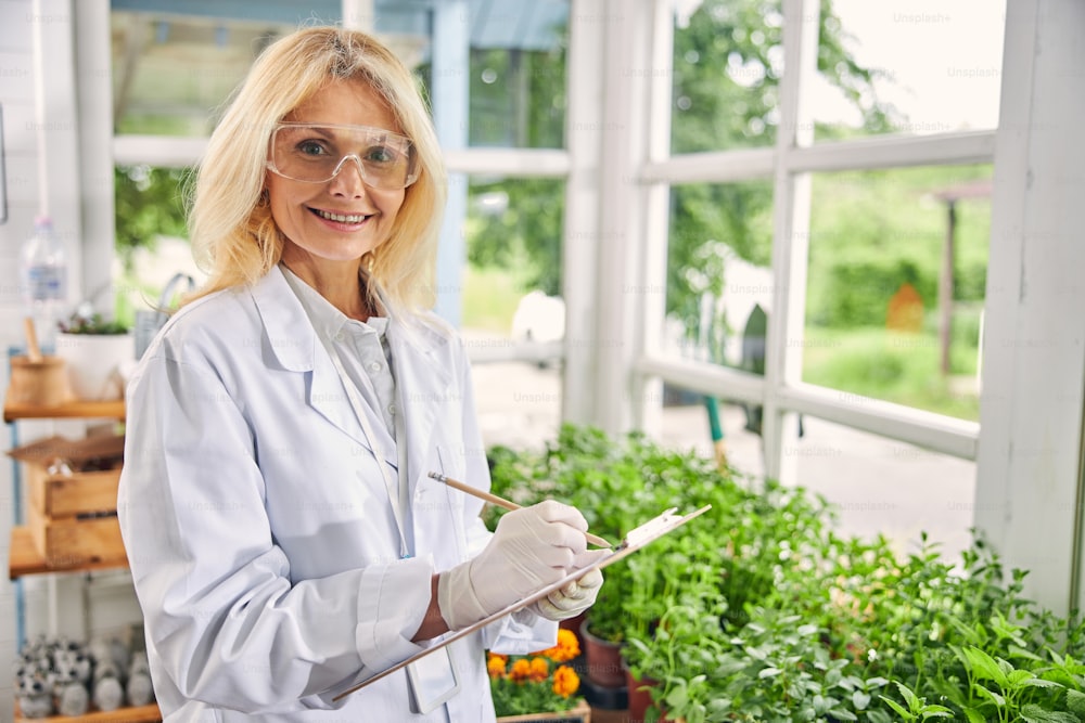 Vista frontale di una biologa sorridente e attraente che indossa occhiali di sicurezza e guanti in lattice monouso