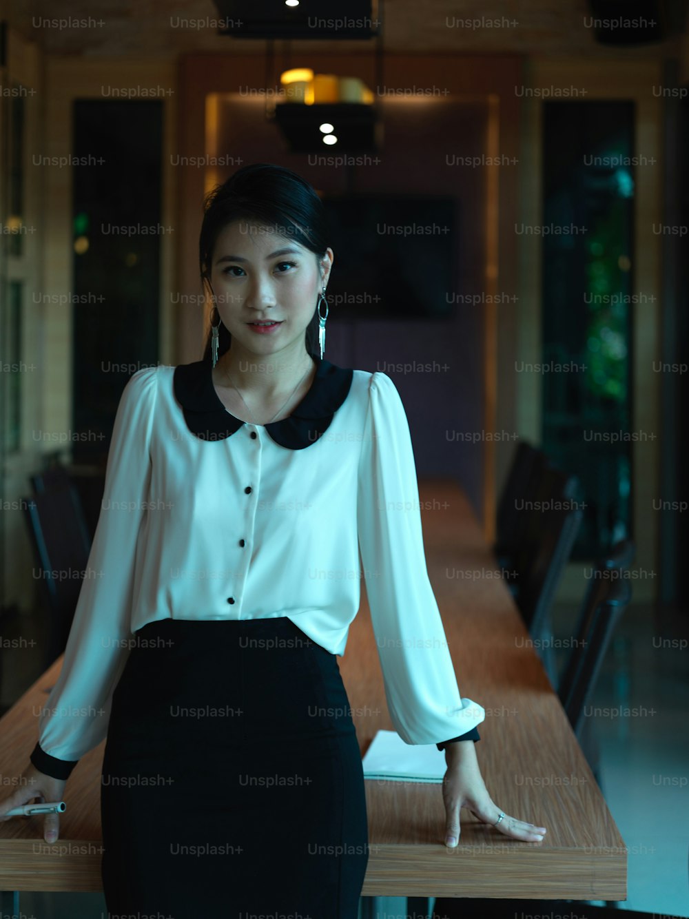 Porträt einer Geschäftsfrau, die lächelt, während sie gegen den Besprechungstisch im luxuriösen Konferenzraum steht