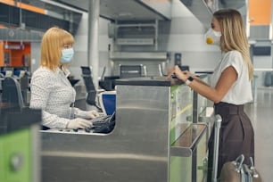 Charming young female person wearing protective mask while being in the airport and doing registration of her boarding pass
