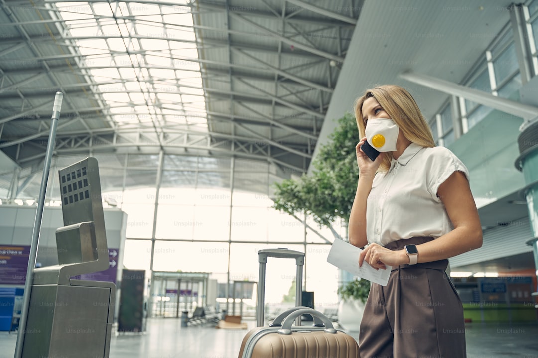 Delighted young female talking per telephone while waiting for her colleague to have business trip together