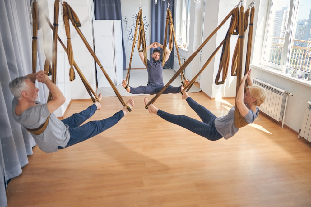 Three people with raised arms and their feet in the stirrups exercising in the hammocks